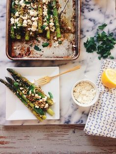 asparagus on a plate with lemon and parsley next to a baking dish