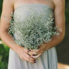 a woman in a gray dress holding a bouquet of silver flowers with her hands on her hips