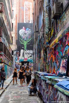 people walking down an alleyway with graffiti on the walls