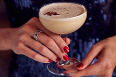 a woman holding a drink in her hand with red nail polish on it and a ring