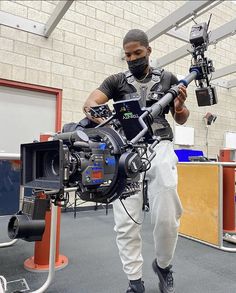 a man standing in front of a camera on top of a tripod holding a laptop