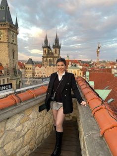 a woman standing on top of a building next to a clock tower with her legs crossed