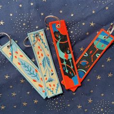 three different key chains are laying on a blue surface with stars and small white stars in the background