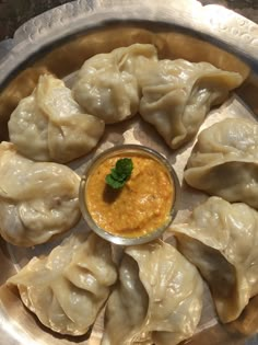 some dumplings are sitting on a silver plate with a small sauce in the middle