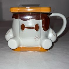 a coffee cup shaped like a dog with a yellow top and brown nose is sitting on a white surface