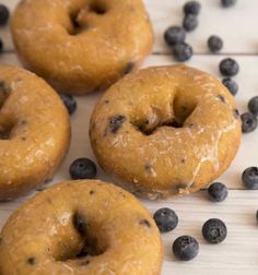 four blueberry donuts on a white wooden surface with fresh blueberries scattered around them