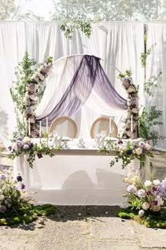 an outdoor ceremony setup with flowers and greenery on the table, along with two wicker chairs