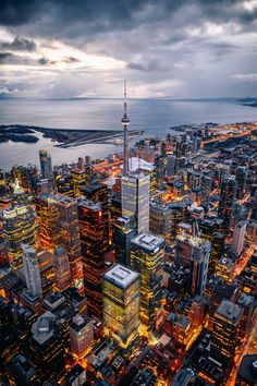 an aerial view of the city lights and skyscrapers at night, with water in the background