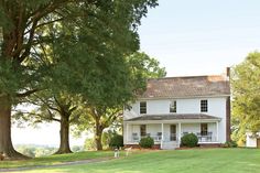 a large white house sitting in the middle of a lush green field next to trees