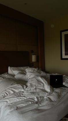 an unmade bed in a hotel room with a laptop computer on the end of it