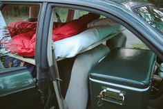 the back seat of a car filled with luggage and blankets, next to an open trunk