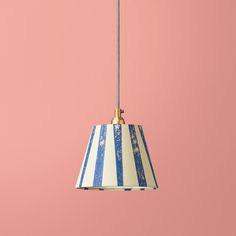 a blue and white striped lamp hanging from a pink wall with a gold metal hook