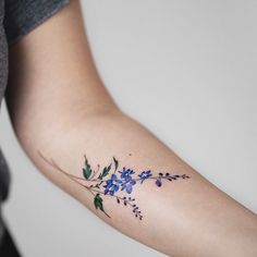 a woman's arm with blue flowers and green leaves on the left side of her arm