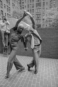 two people are dancing on the sidewalk in front of tall buildings