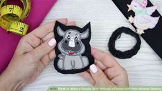 a person is holding a small animal brooch with scissors next to it and measuring tape