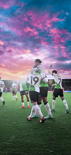 a group of soccer players huddle together on the field during a game at sunset