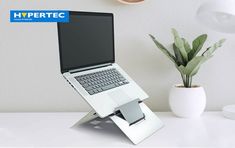 an open laptop computer sitting on top of a white desk next to a potted plant