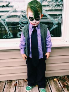 a young boy dressed as the joker standing on a wooden deck in front of a window