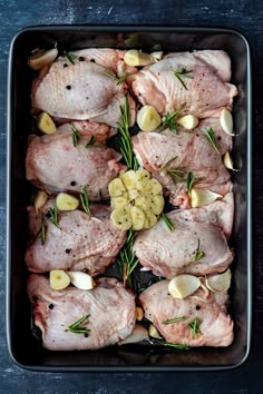 raw chicken in a baking dish with garlic and rosemary garnishes on the side