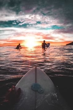 two people in the water with surfboards at sunset