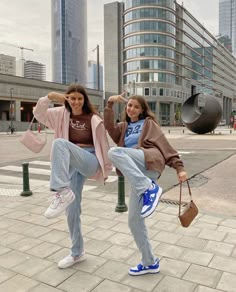 two young women are posing on the sidewalk in front of some buildings and one is holding her leg up