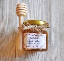 a honey jar with a wooden spoon and label on the lid sitting on a table