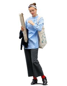 a woman in blue shirt and grey pants holding a bag with her hand on it