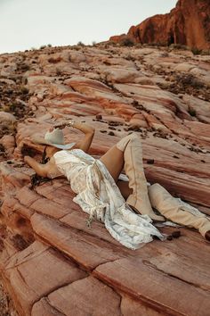 a woman laying on top of a rock covered in dirt next to a desert landscape