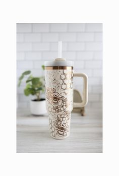 a white and gold coffee cup sitting on top of a table next to a potted plant