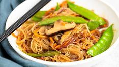 a white bowl filled with noodles, mushrooms and green peppers next to chopsticks