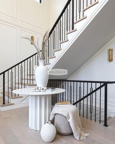 a white vase sitting on top of a table next to a stair case in a house