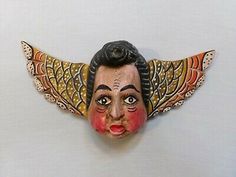 an old mask with wings on it's head and eyes painted red, orange, yellow and black