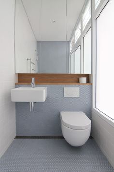 a white toilet sitting next to a bathroom sink under a mirror in a room filled with windows