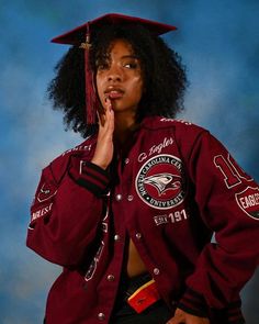 a woman wearing a maroon jacket and hat with her hand in her mouth while standing against a blue background