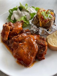 a white plate topped with meat covered in sauce next to bread and lettuce