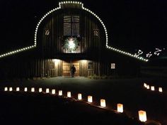 there are many lit candles in front of a barn with lights on the roof and windows