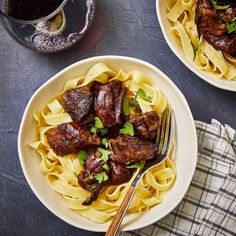 two plates of pasta with meat and sauce on the side next to a glass of wine