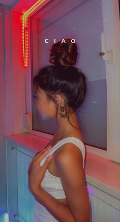 a woman standing in front of a mirror with her back turned to the camera and wearing a white tank top