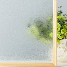 a vase filled with green flowers next to a frosted glass window covered in condensation