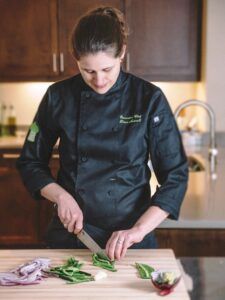 a woman cutting up vegetables on top of a wooden table