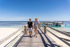 two people walking down a pier towards the ocean