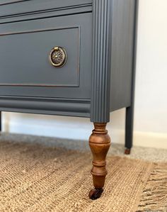 a gray dresser with brass knobs on it's handles and drawers, sitting on a carpeted floor