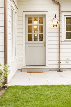 a white house with a light on the front door and green grass in front of it