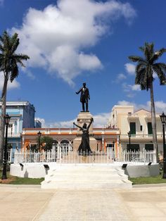 there is a statue in front of the building with palm trees around it and a blue sky