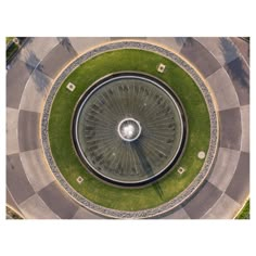 an aerial view of a circular fountain in the middle of a park with green grass