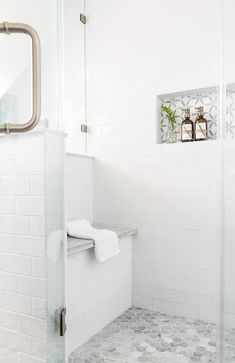 a white tiled bathroom with a glass shower door and toilet paper roll holder on the wall