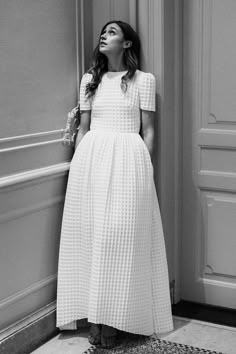 a woman in a white dress leaning against a wall