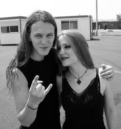 two young women standing next to each other in front of a parking lot holding their fingers up