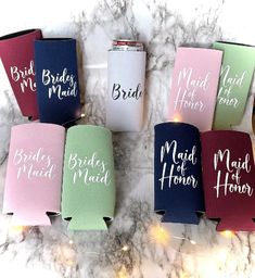 six bridesmaid flasks in different colors on a marble countertop with fairy lights