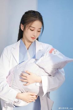 a woman in a white lab coat holding a stuffed animal on her chest and looking down at the ground